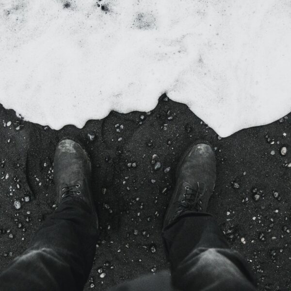 Grayscale shot of dirty shoes standing on the sandy beach with waves