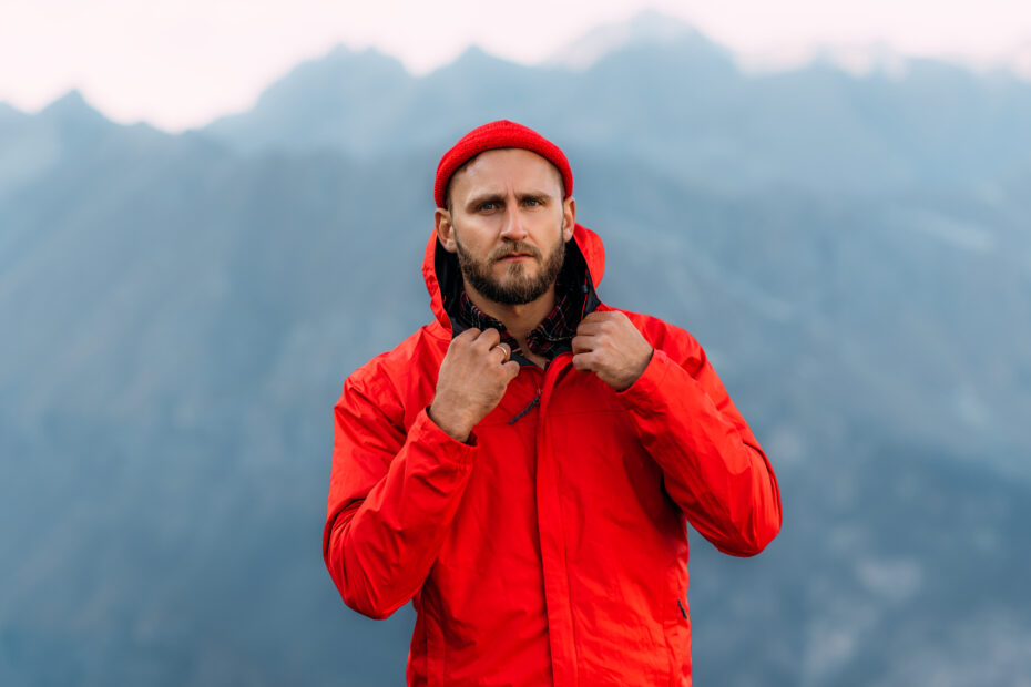 Portrait of a brutal bearded man in a red jacket and hat among the mountains